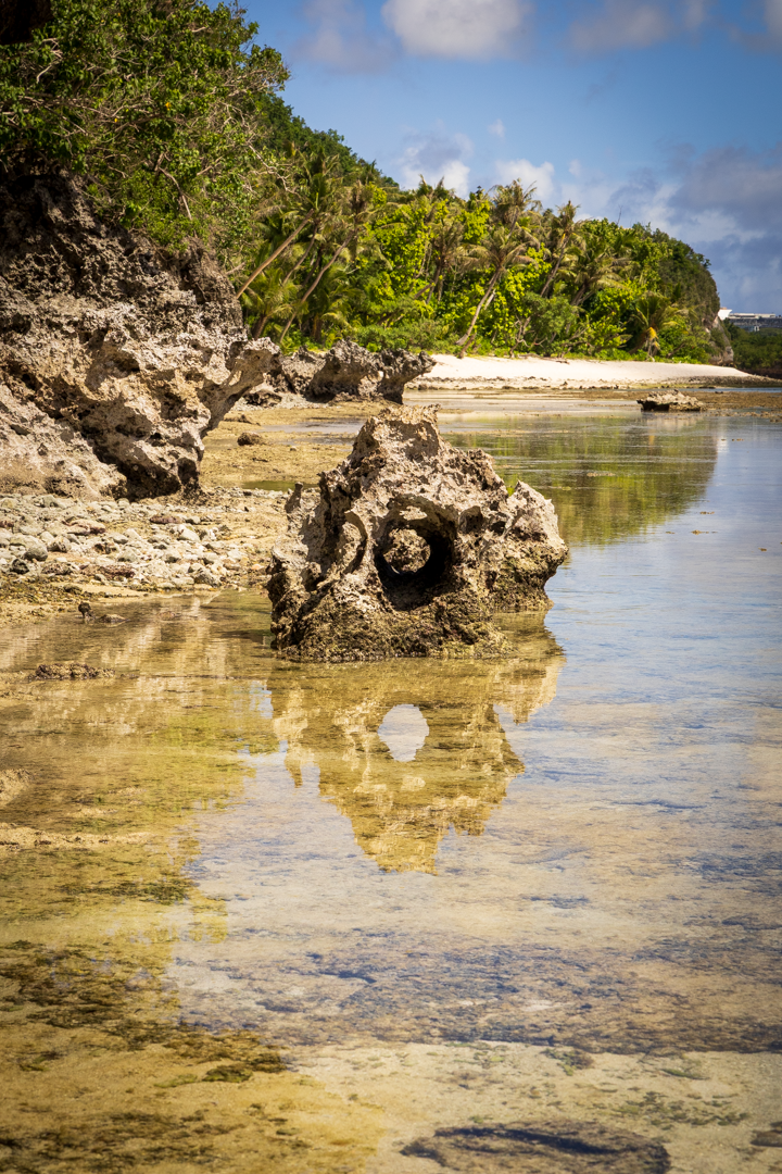 Fine art landscape photo of a weathered limestone rock formation at Gun Beach, Guam, reflecting the blue sky in a still tide pool.