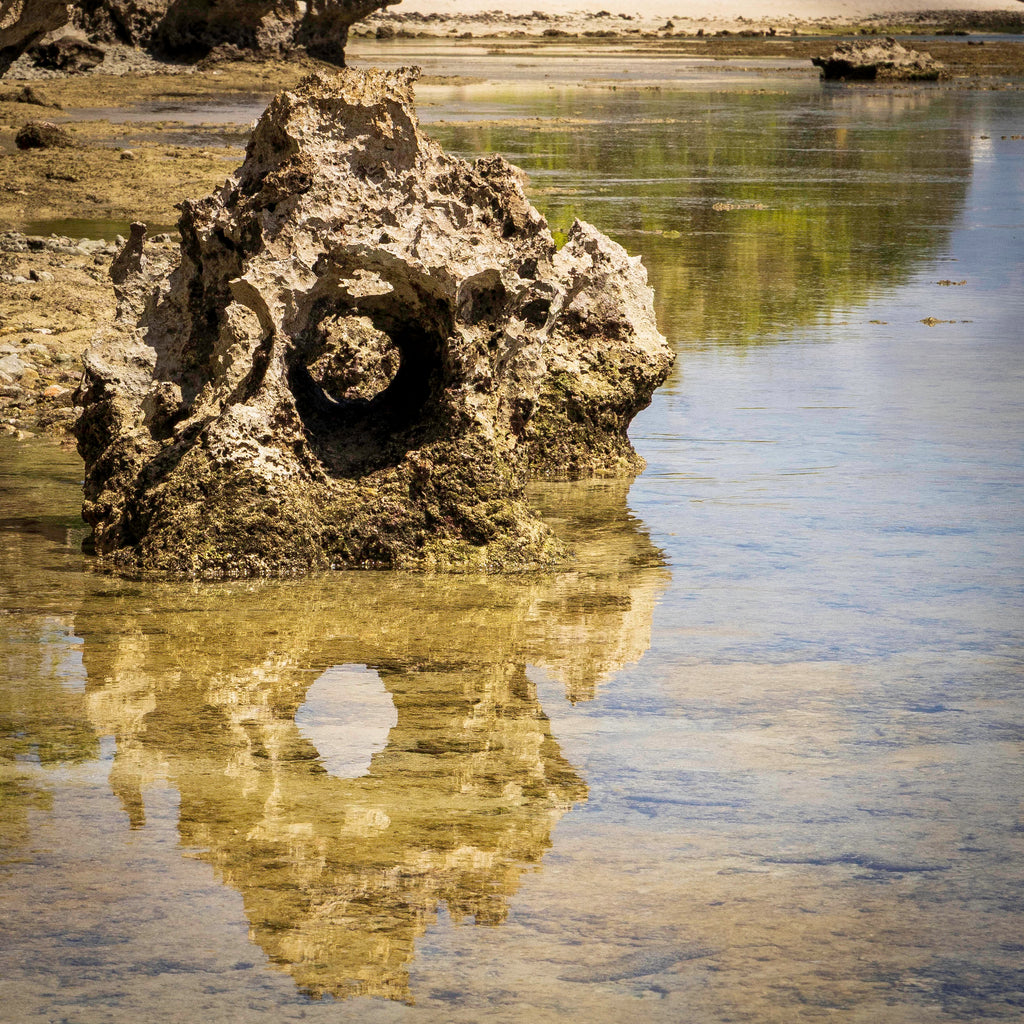 A close-up detail shot focusing on the crisp mirror reflection of weathered limestone coast textures in calm, crystal-clear water.
