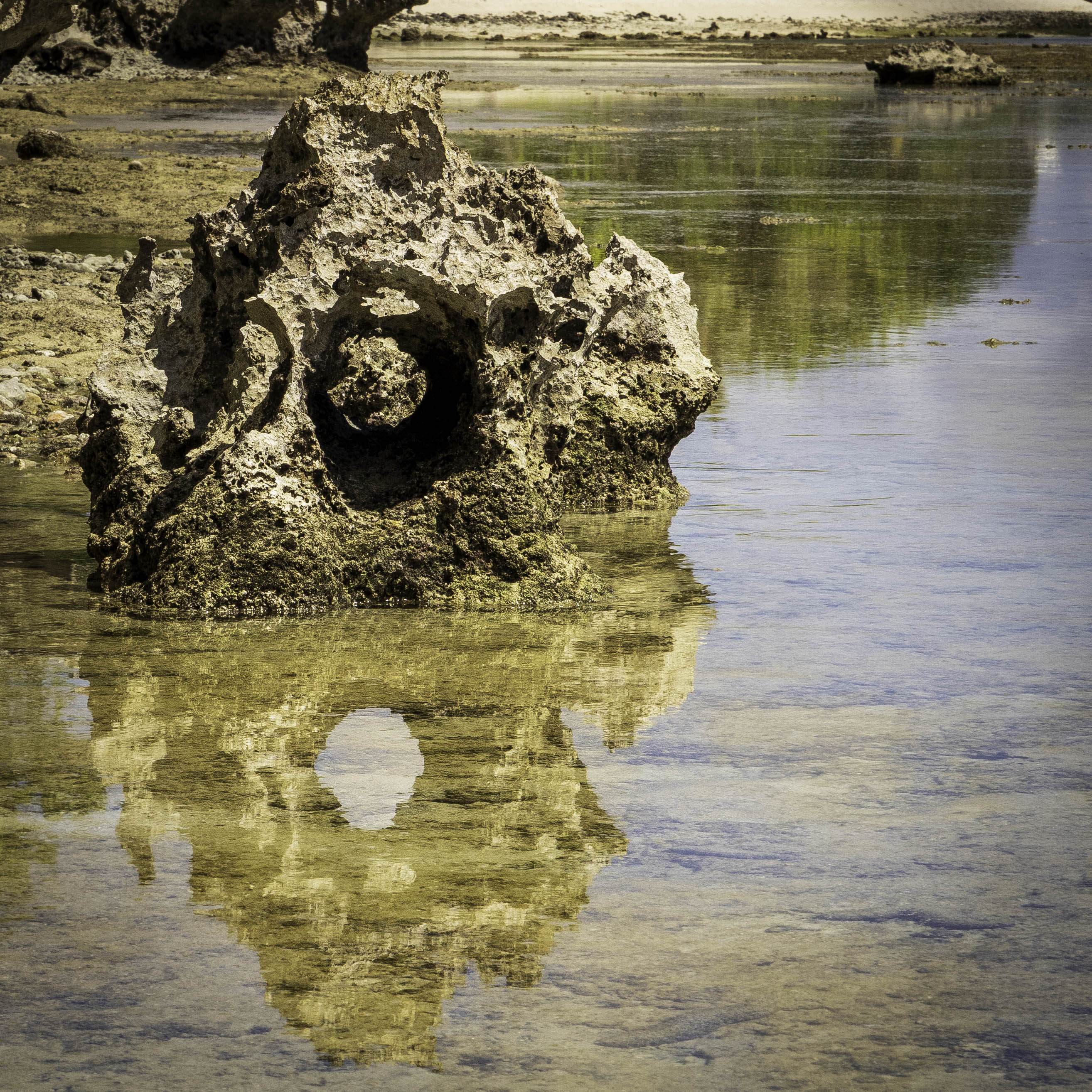 A close-up detail shot focusing on the crisp mirror reflection of weathered limestone coast textures in calm, crystal-clear water.