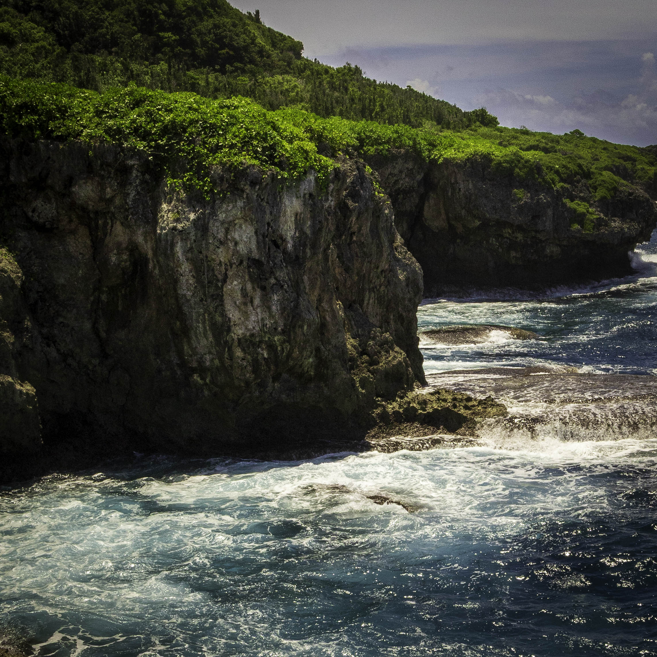 A close-up view highlighting the sharp, porous texture of coastal volcanic limestone formations against churning blue seawater.