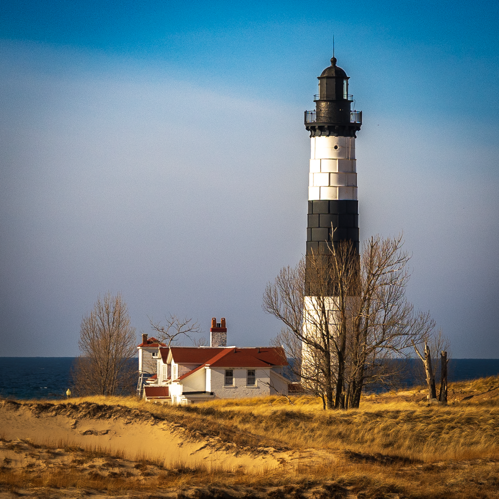 A close-up detail shot highlighting the black and white striped tower and red-roofed keeper house of Big Sable Point Lighthouse.
