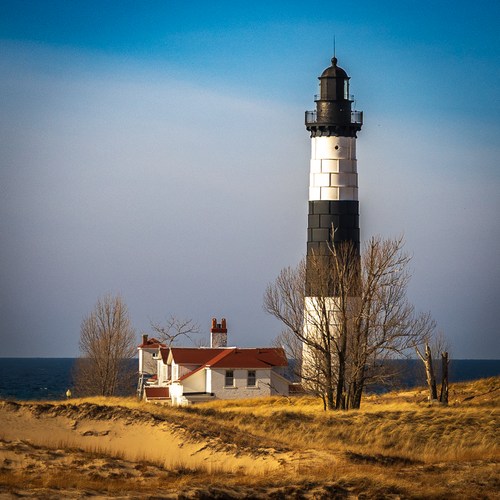 A close-up detail shot highlighting the black and white striped tower and red-roofed keeper house of Big Sable Point Lighthouse.