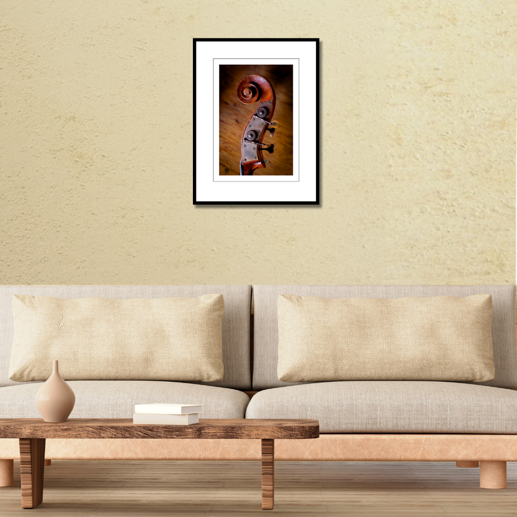A framed fine art macro print of an upright bass scroll displayed on a living room wall over a couch to demonstrate scale.