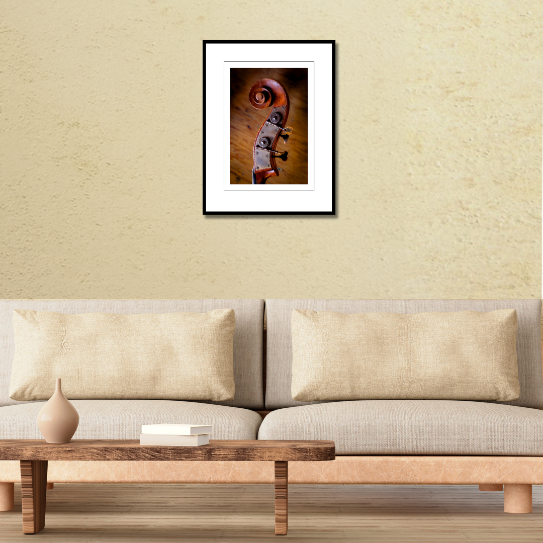 A framed fine art macro print of an upright bass scroll displayed on a living room wall over a couch to demonstrate scale.