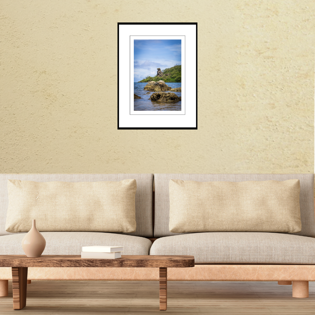 A framed fine art coastal print of Bear Rock in Guam displayed on a living room wall above a couch to show scale.