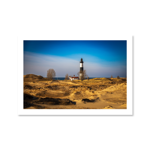 Landscape view of the historic black and white Big Sable Point Lighthouse rising above rolling golden sand dunes in Michigan.