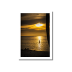 Vibrant golden sunset with dramatic clouds reflecting on calm water, featuring a silhouette of a lone paddleboarder in the distance.