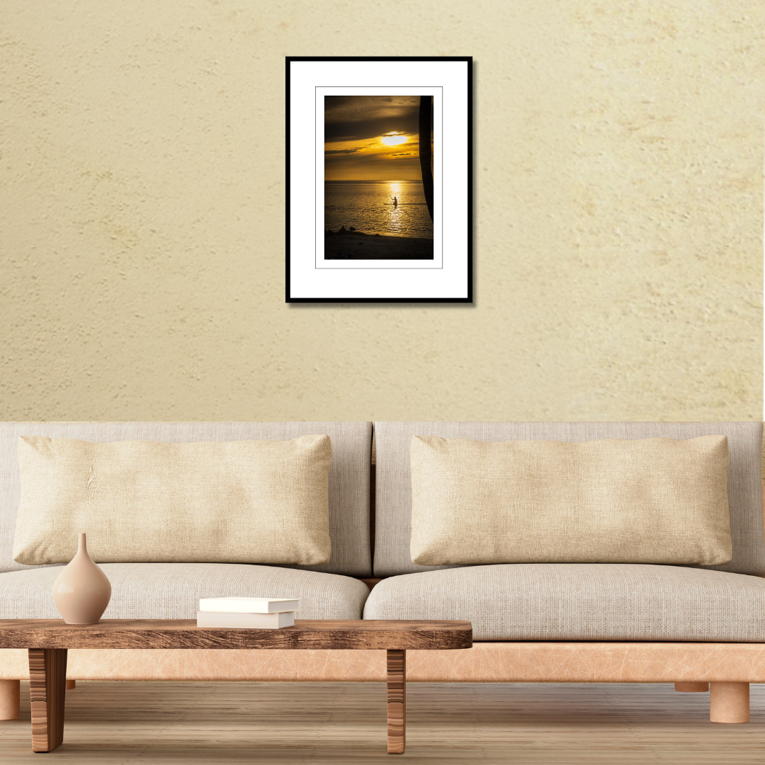 A framed fine art sunset print displayed on a modern living room wall over a couch to demonstrate scale.