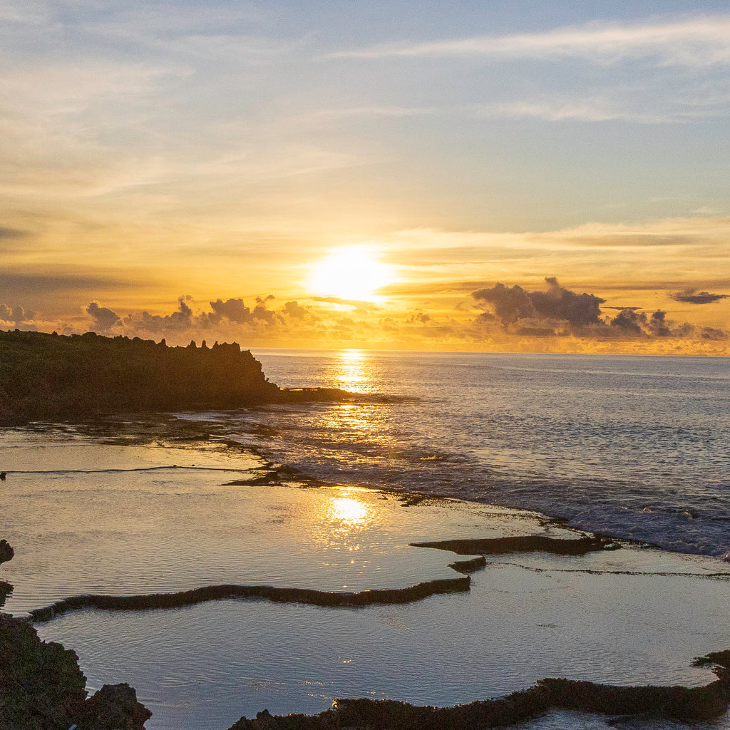 A close-up detail view of the golden sunrise reflecting over the calm tide pools and weathered limestone karst formations in Guam.
