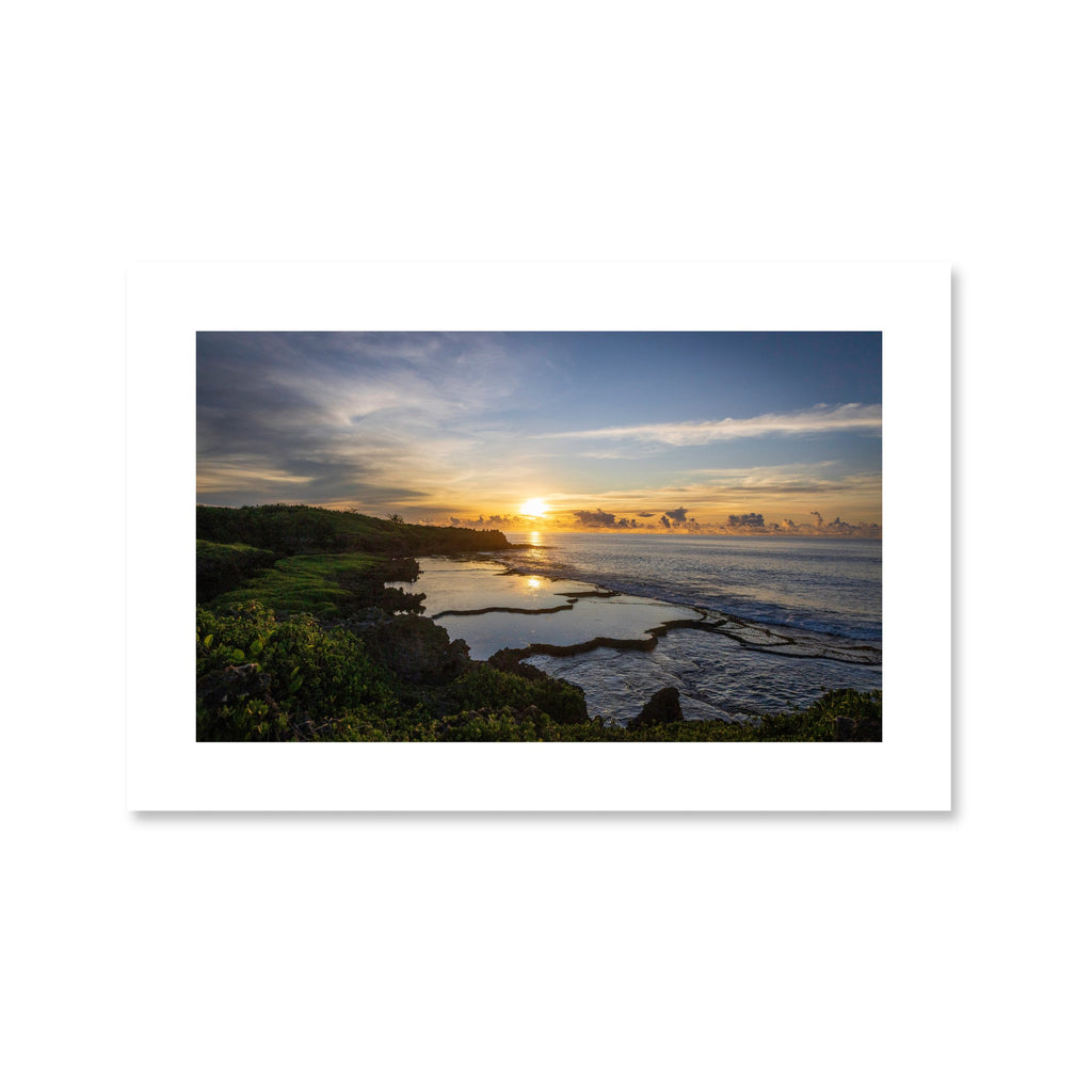 A serene sunrise over the Inalåjan Natural Pools in Guam, with the golden sun reflecting perfectly on the still, turquoise tide pools.