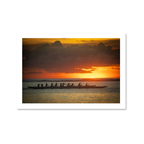 A striking silhouette of a traditional outrigger canoe team paddling across calm ocean waters during a vibrant golden sunset.