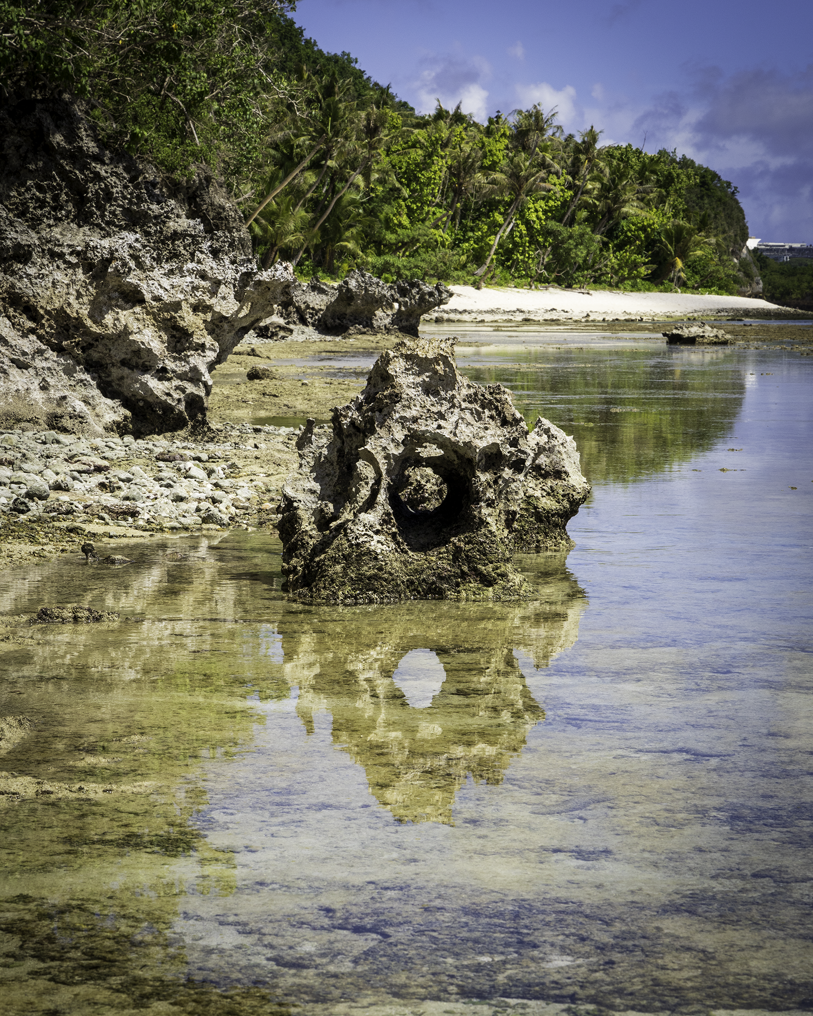 "Fine art landscape photograph of a limestone rock formation in Guam reflecting the blue sky in a clear tidal pool at Gun Beach."