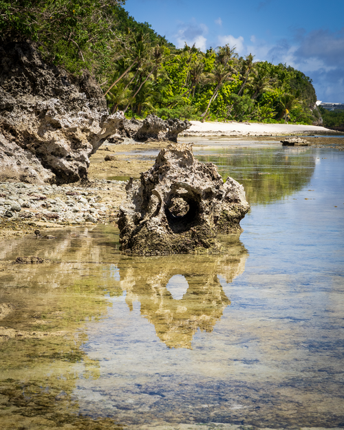 "Fine art landscape photograph of a limestone rock formation in Guam reflecting the blue sky in a clear tidal pool at Gun Beach."