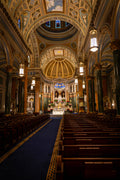 Interior view of St. Jean Baptiste Church in NYC featuring ornate golden lighting, symmetrical wooden pews, and Renaissance Revival architecture.