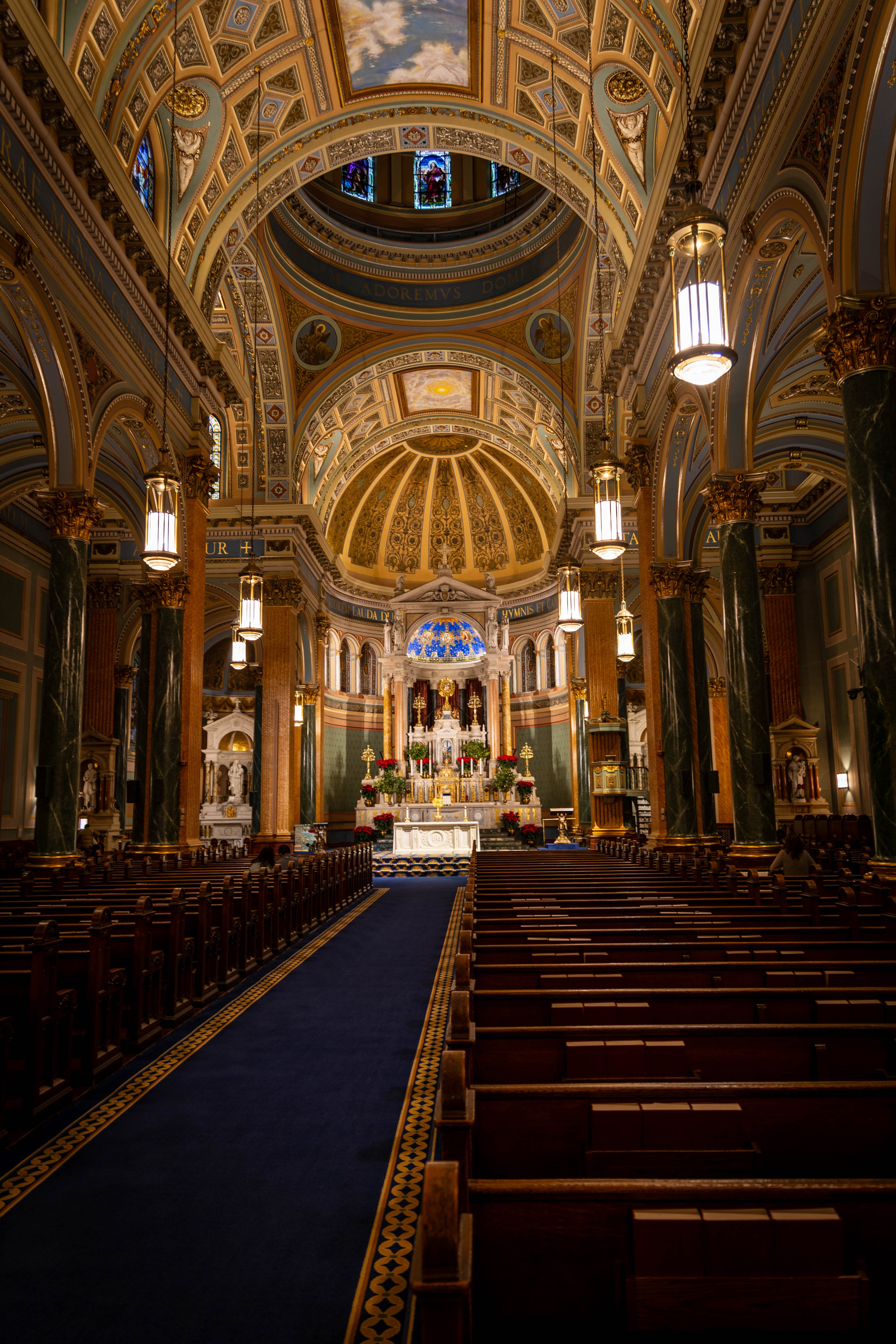 Interior view of St. Jean Baptiste Church in NYC featuring ornate golden lighting, symmetrical pews, and Renaissance Revival architecture during a winter storm.