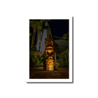A hand-carved wooden tiki totem dramatically illuminated by ground uplighting along a resort pathway at night in Tumon Bay Guam.
