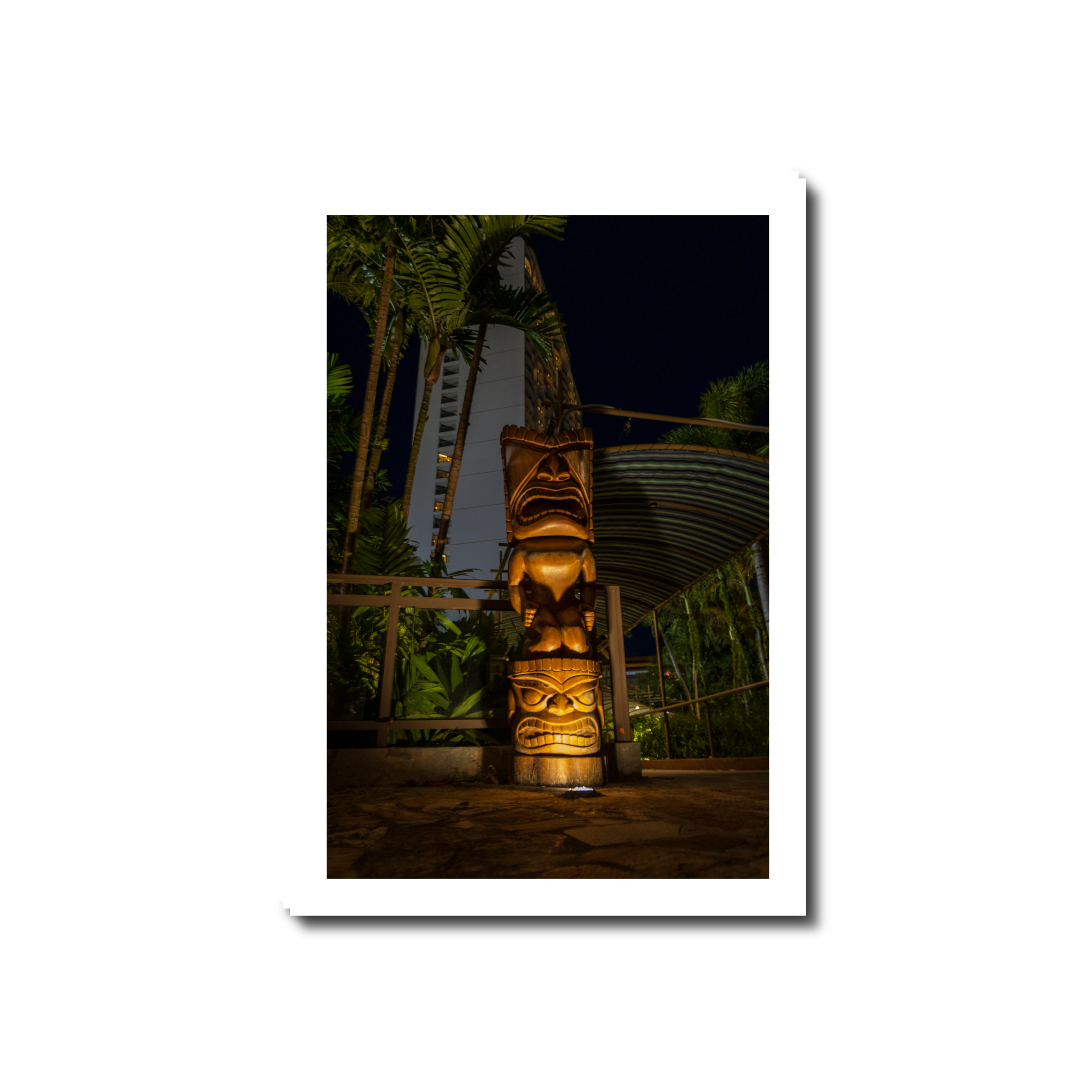 A hand-carved wooden tiki totem dramatically illuminated by ground uplighting along a resort pathway at night in Tumon Bay Guam.