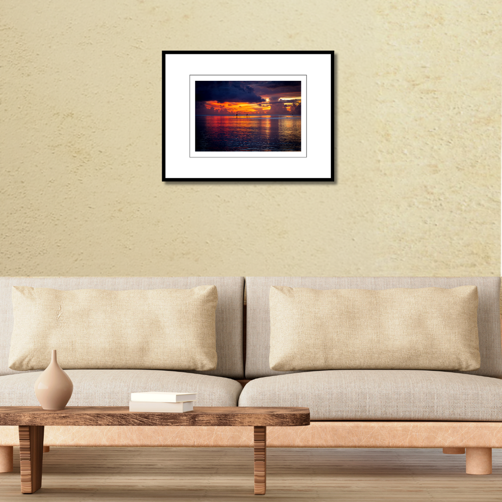 A 18x12 Tumon Bay Sunset print in an 24x18 frame, styled on a living room wall above a contemporary couch.